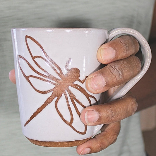 White ceramic mug with dragonfly stencil in hand