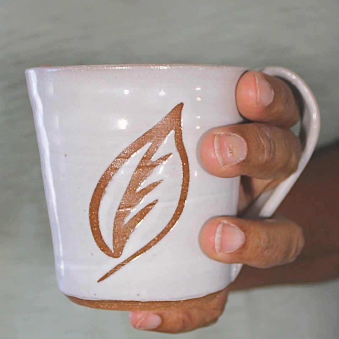 White ceramic mug with leaf stencil in hand