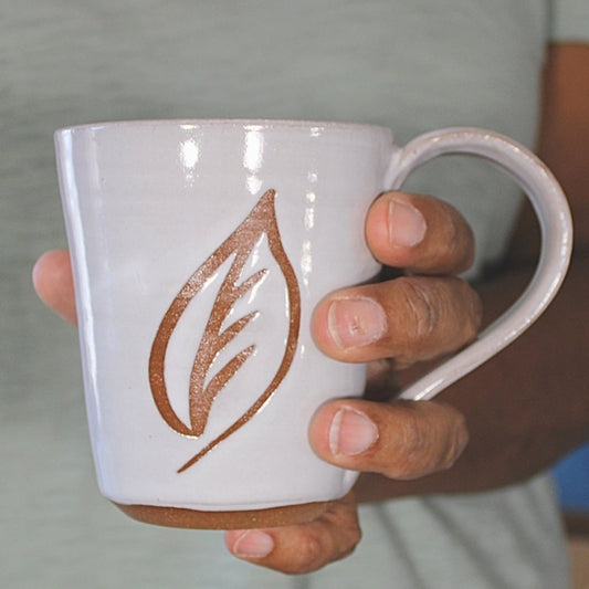 White ceramic mug with leaf stencil in hand