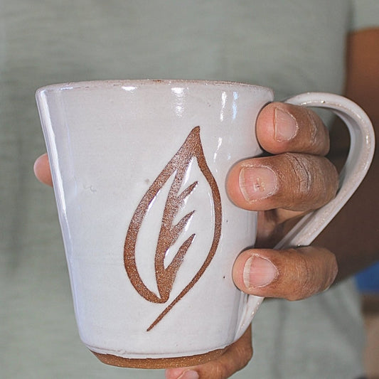 White ceramic mug with leaf stencil held in hand