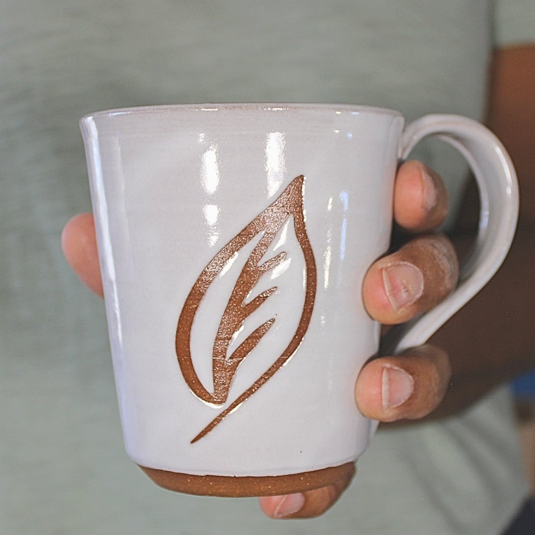 White ceramic mug with leaf stencil in hand